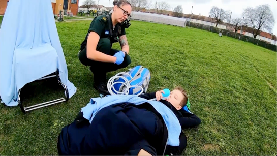Paramedic kneeling next to injured boy in field