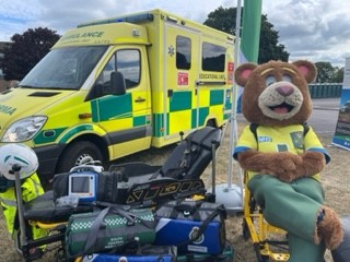 SCAS mascot 999 Ted sitting next to an ambulance vehicle