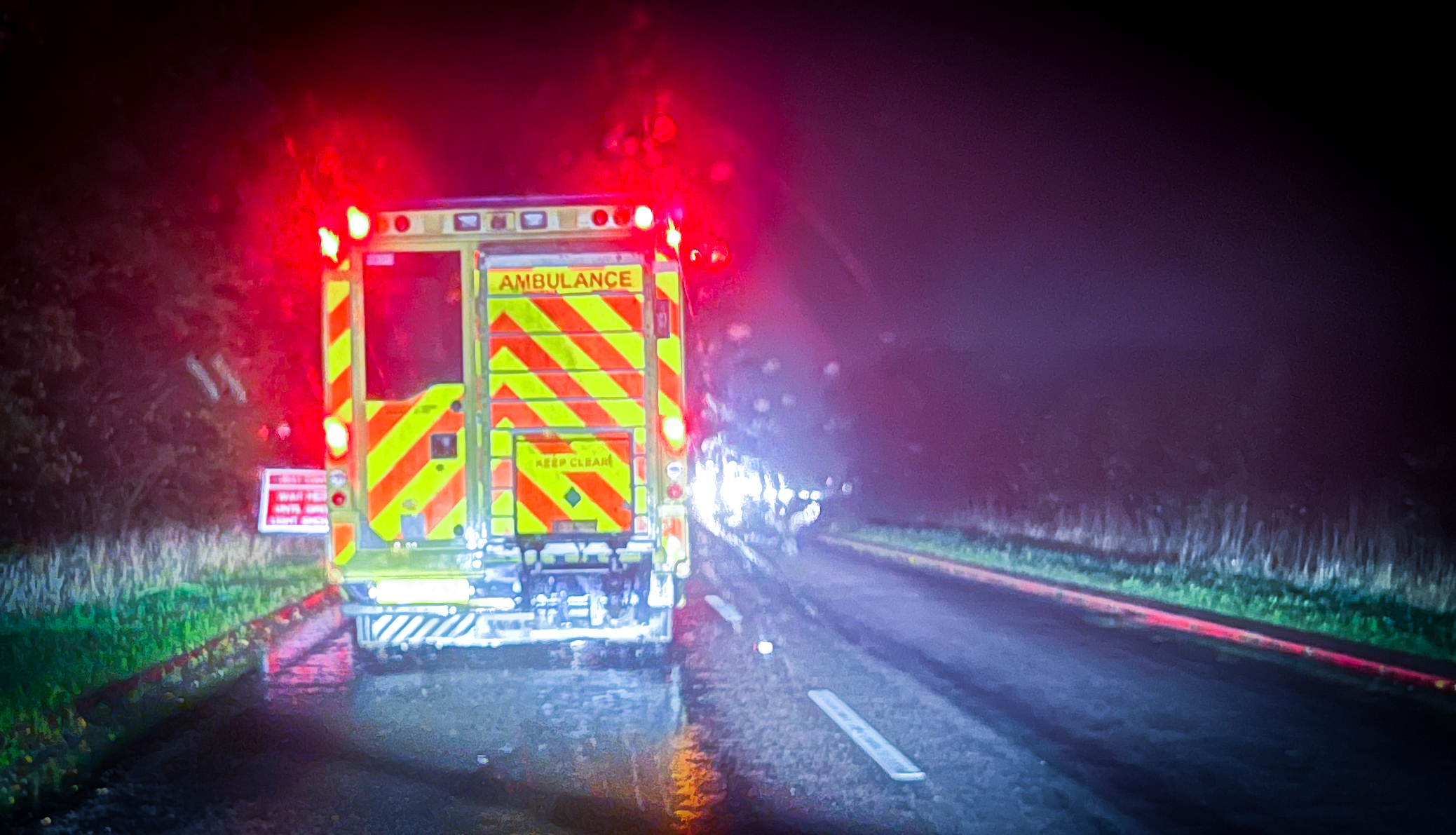 An ambulance parked by the side of the road at night.