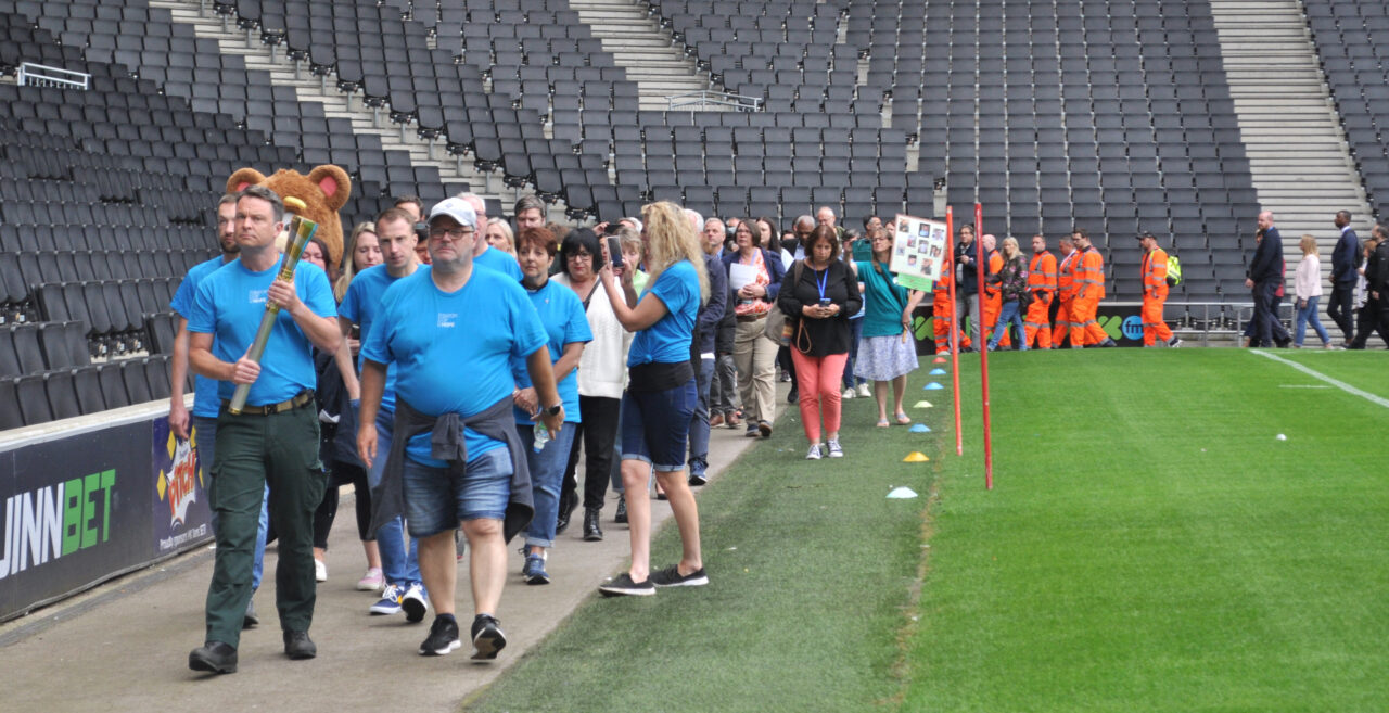 A line of people walk in procession around the perimeter of a football stadium