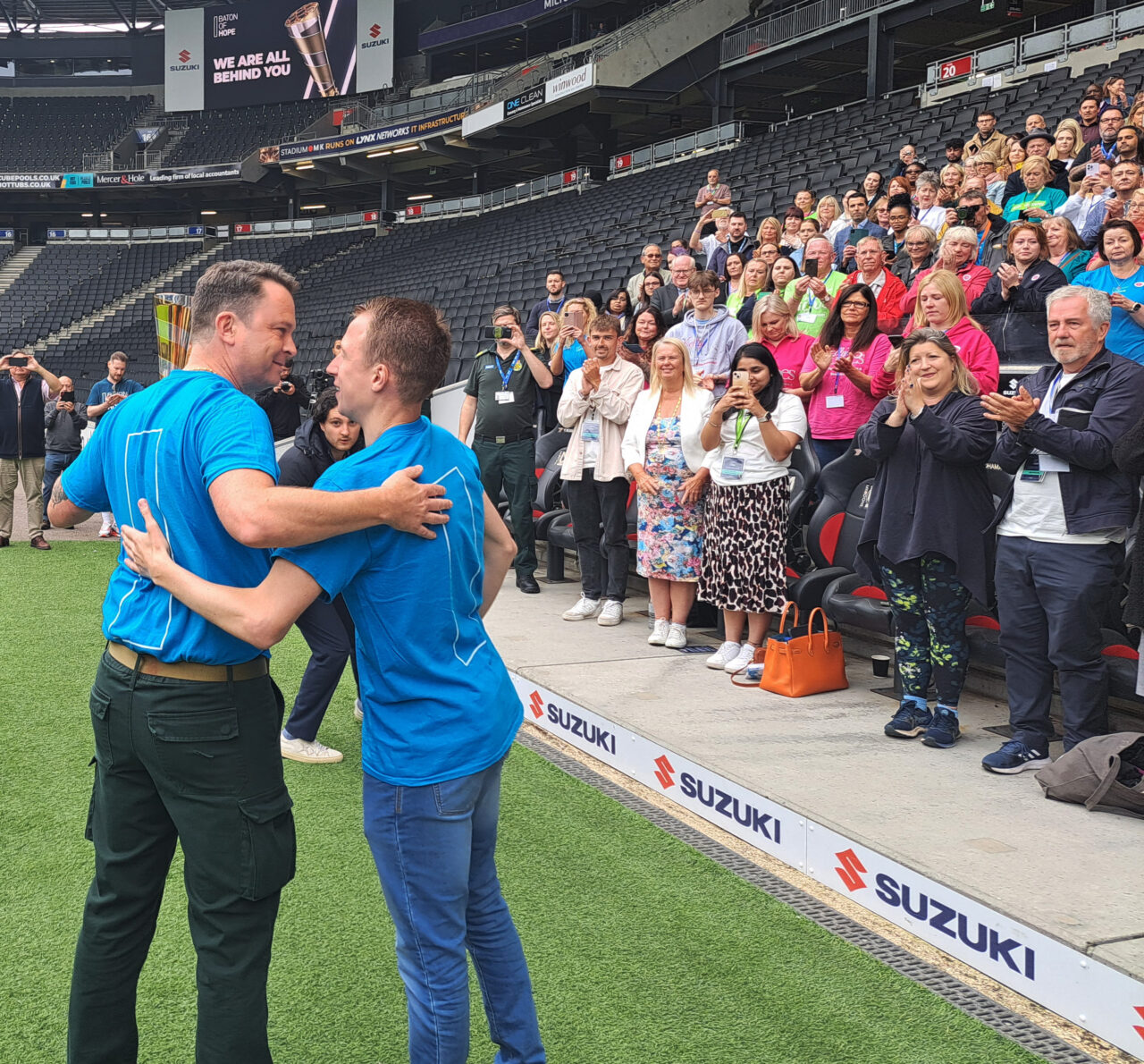 Two men embrace in front of a crowd seated in a football stadium