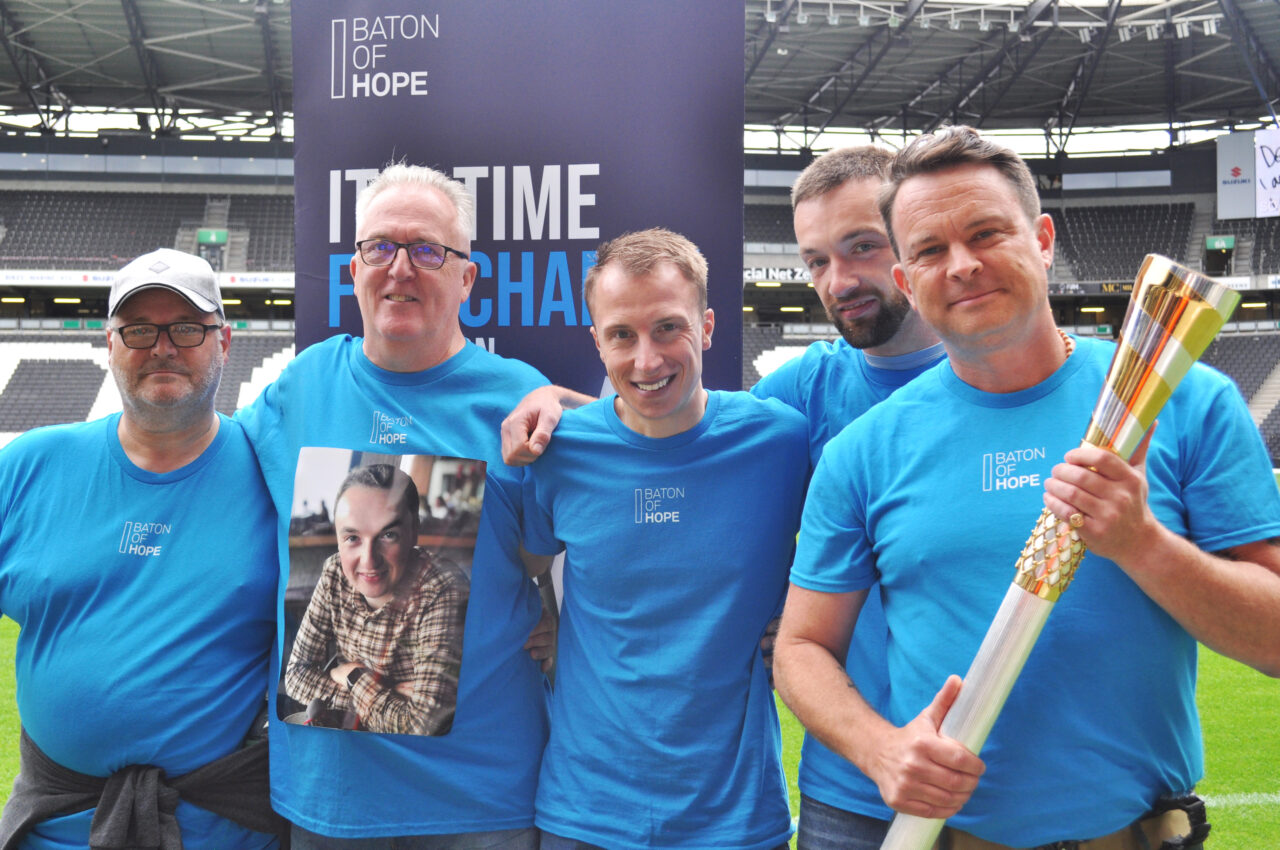 A group of five men standing in a line with one holding the Baton of Hope