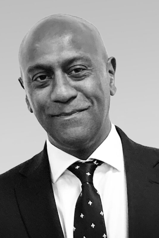 A black and white portrait photo of Daryl Lutchmaya in a suit and tie