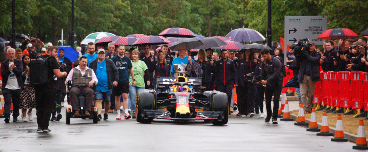 A crowd of people walk behind a Red Bull Racing Formula 1 car