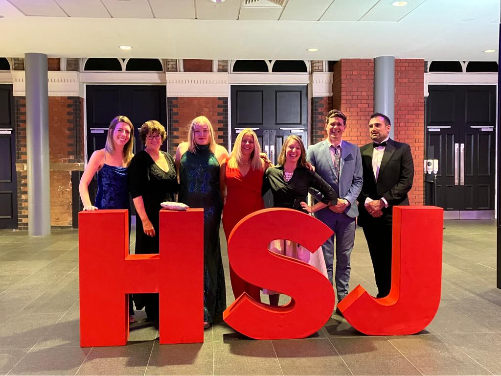 A group of people standing behind the letters H S and J