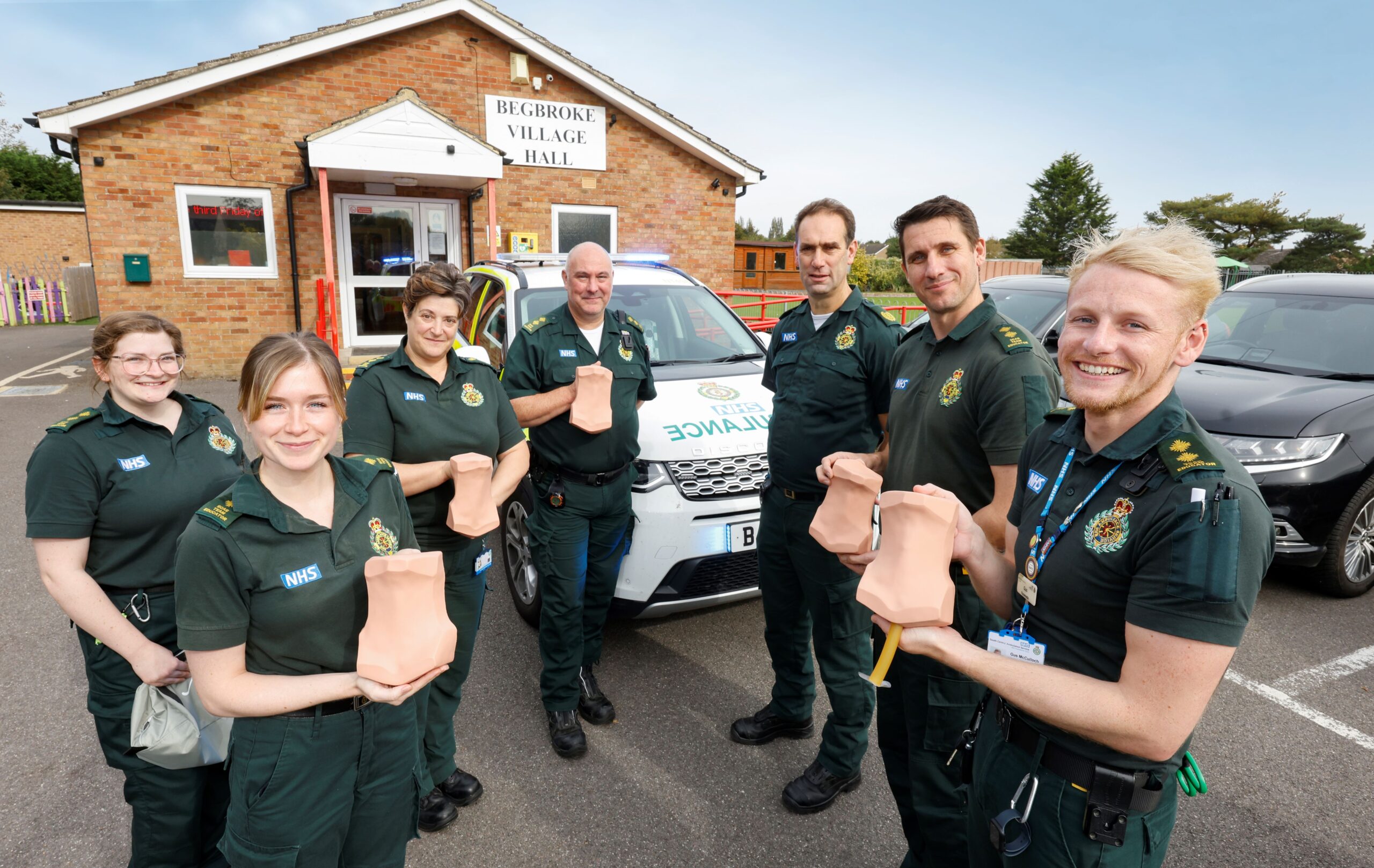 A group of paramedics standing in front of response car holding training aids