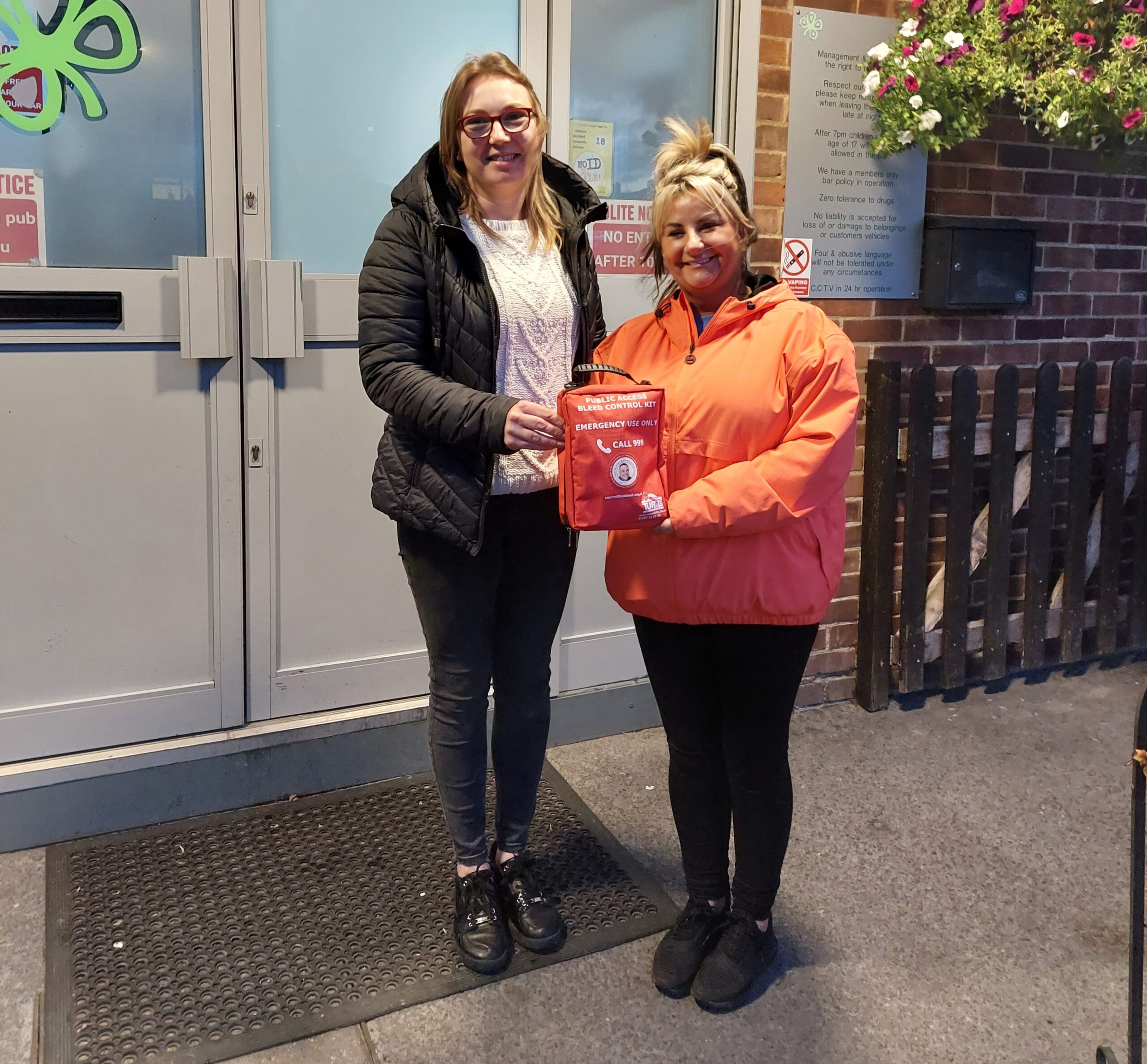 Two people standing outside a building holding an emergency bleed kit