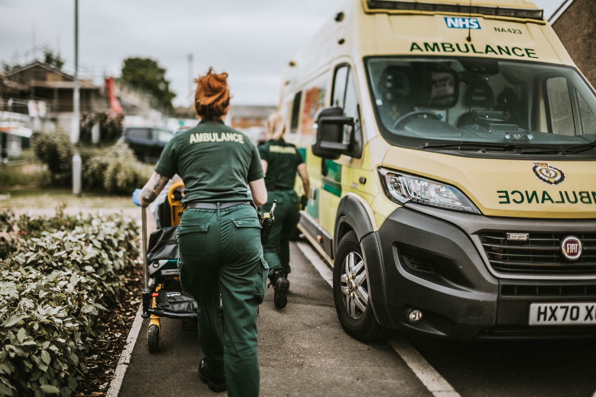 Two ambulance workers push a stretcher towards a parked ambulance