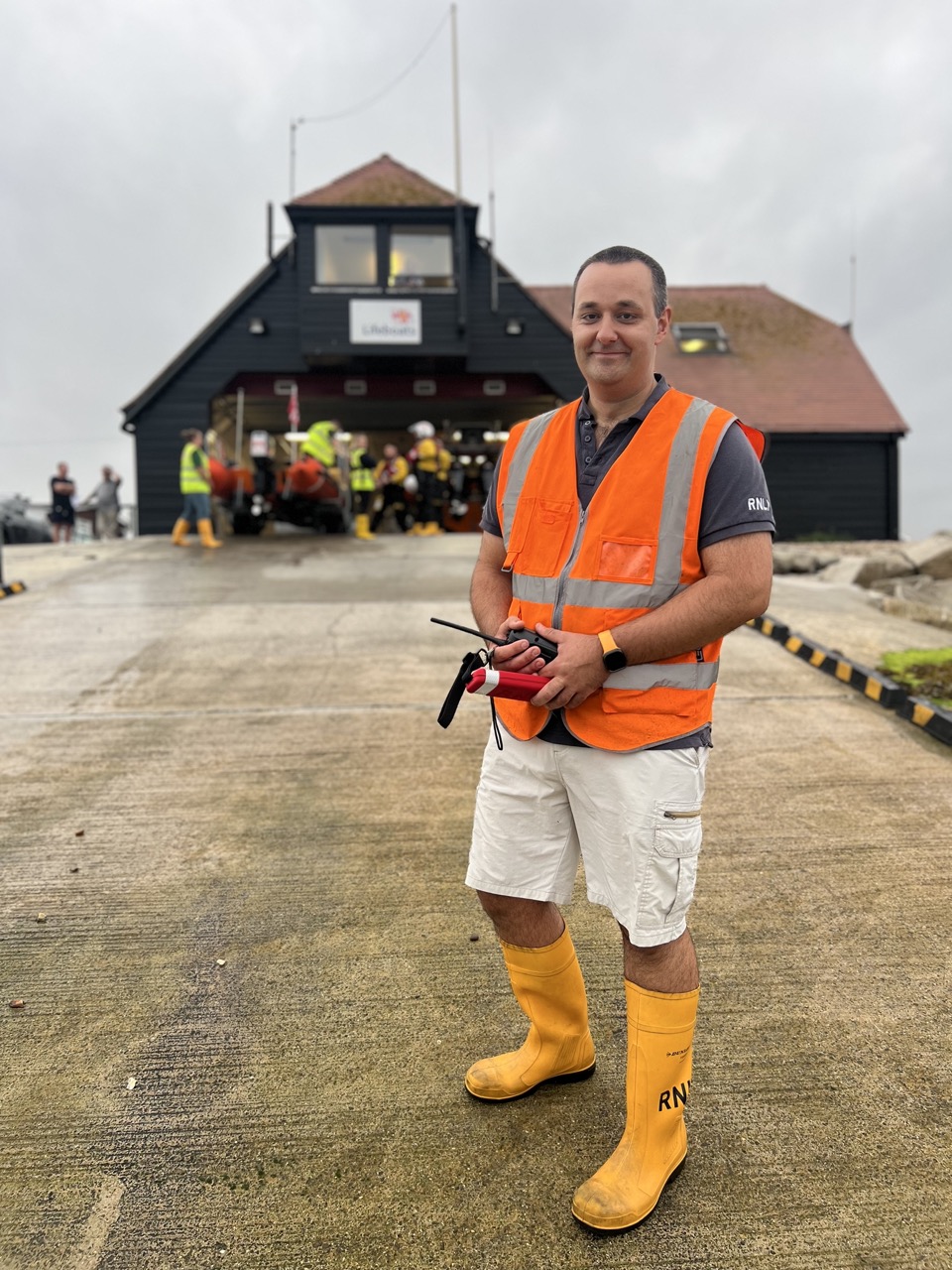 RNLI male volunteer standing on a launch ramp in front of the lifeboat house
