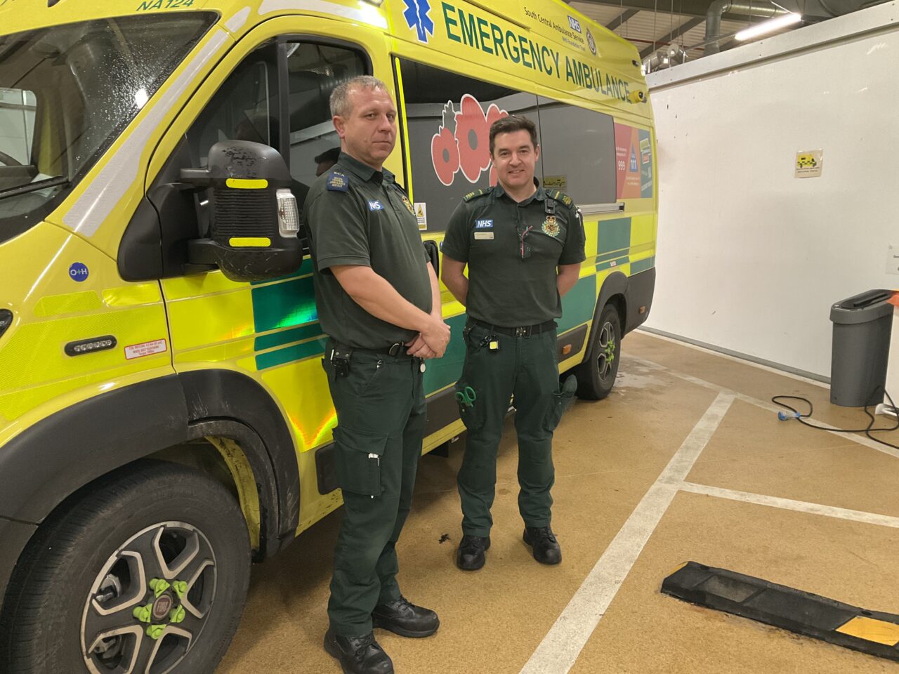 Two male ambulance staff in uniform standing in front of an emergency ambulance