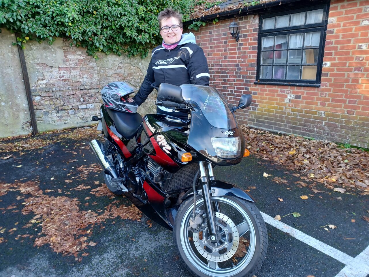 A female motorcyclist in full protective clothing standing behind a Kawasaki motorbike