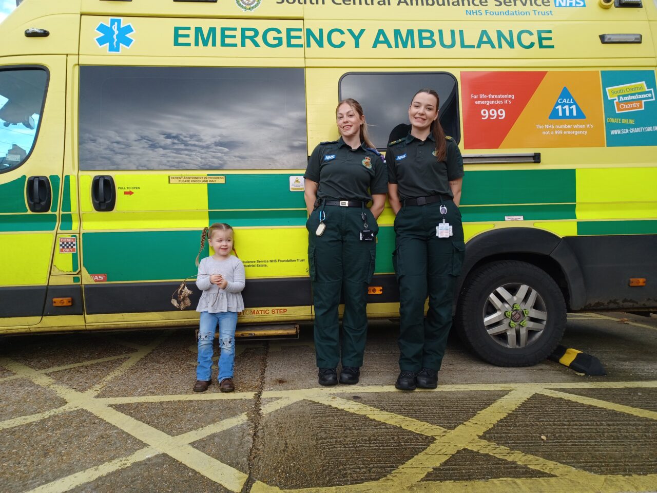 A three-year-old girl standing in front on an ambulance with a female ambulance crew
