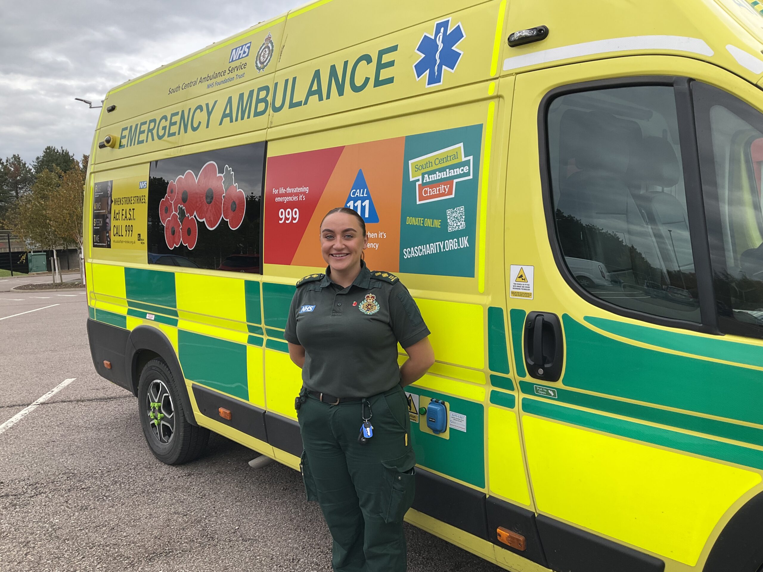 A female paramedic standing in front of a poppy-branded emergency ambulance