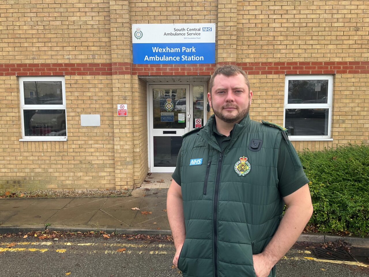 A male paramedic in uniform standing outside the entrance to a building that has the sign Wexham Park Ambulance Station above the entrance