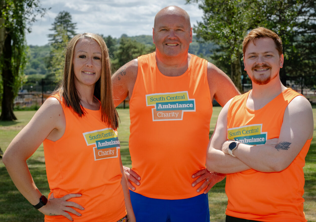 A woman and two men standing outside wearing running vests