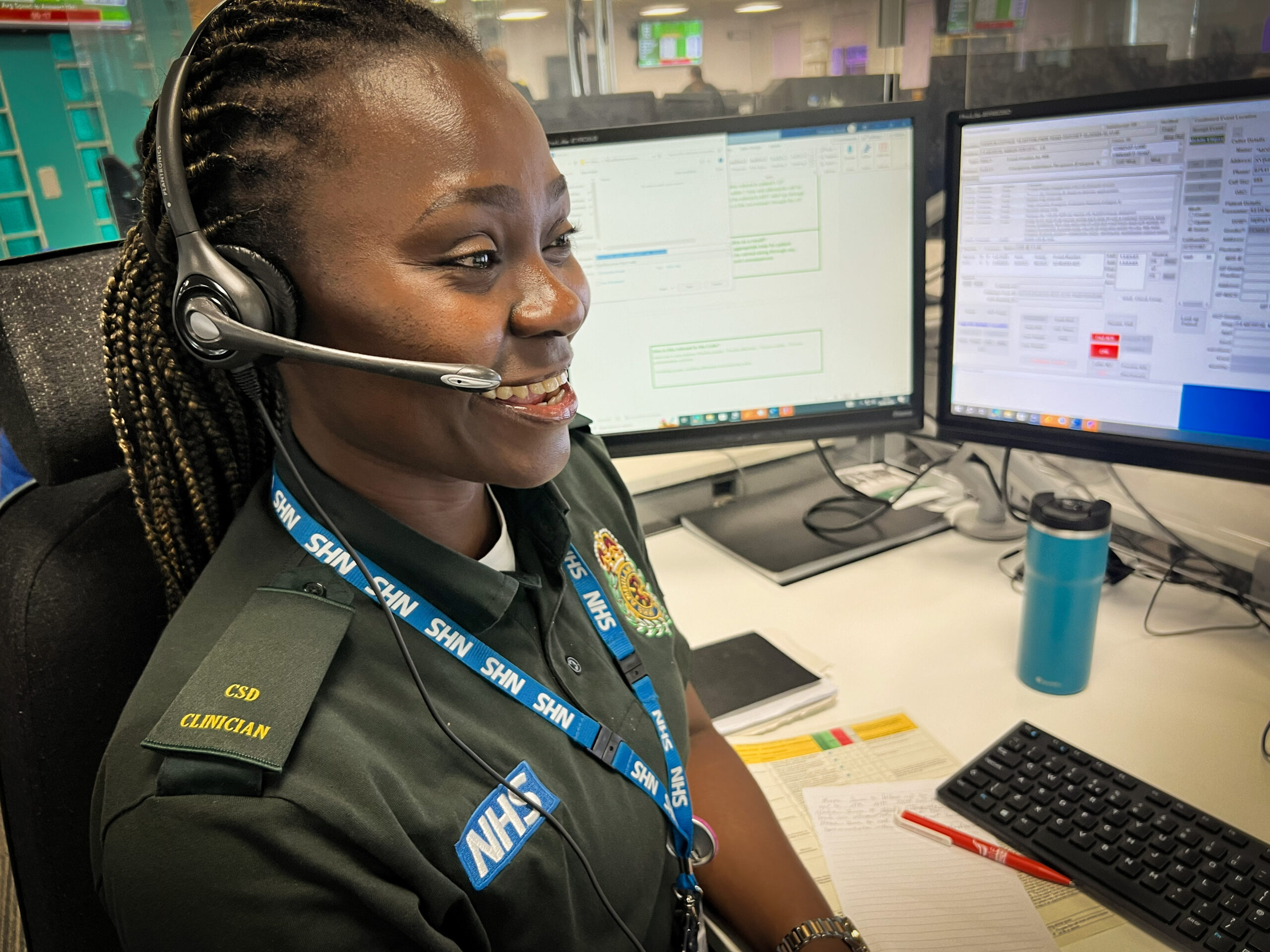 A female clinician in green ambulance uniform working at the clinical support desk in the emergency control room