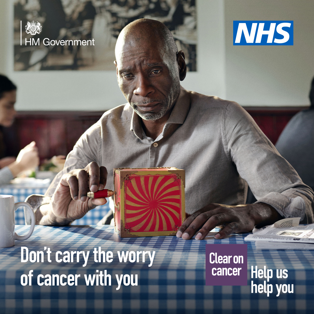 A black male sits at a table looking at a jack-in-the-box. The text in the image reads 'Don't carry the worry of cancer with you'