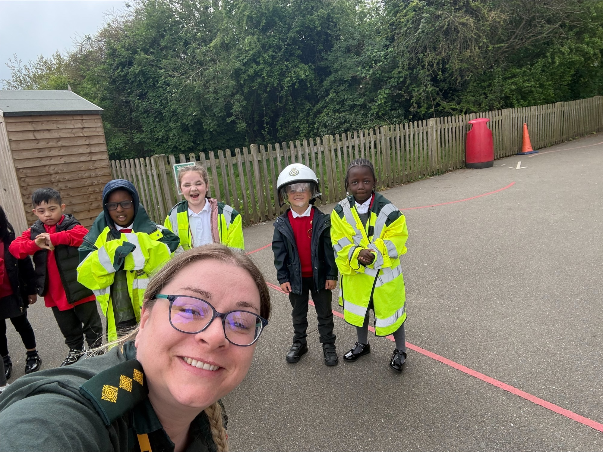 A female paramedic in green uniform taking a selfie with reception class school children wearing ambulance PPE in the background.