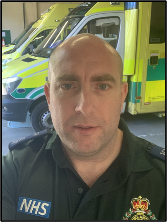A head and shoulders image of a paramedic in uniform standing in front of a row of ambulances