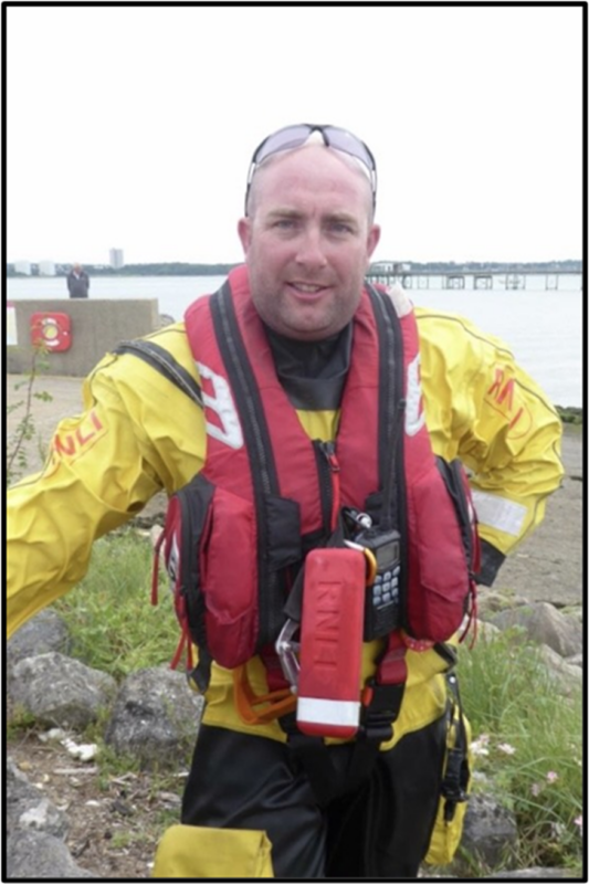 A male RNLI volunteer standing in full kit on the shoreline