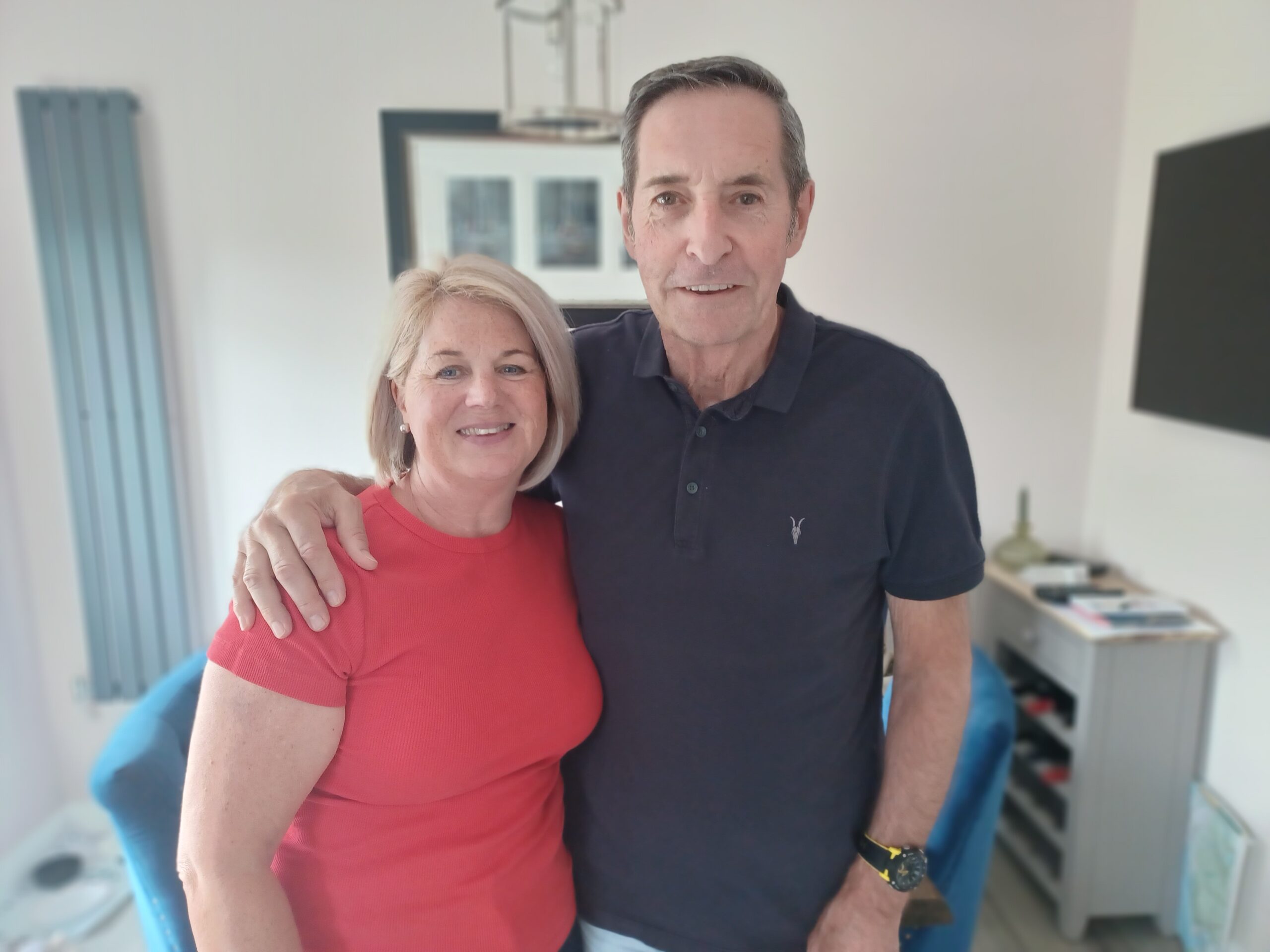 A woman and man in their home standing side by side with their arms around each other