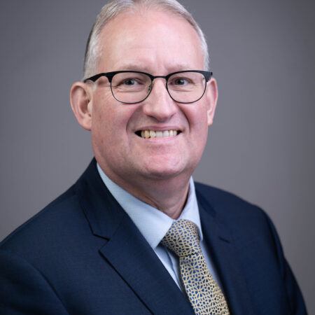 A head and shoulders photo of a man in a suit and tie smiling at the camera