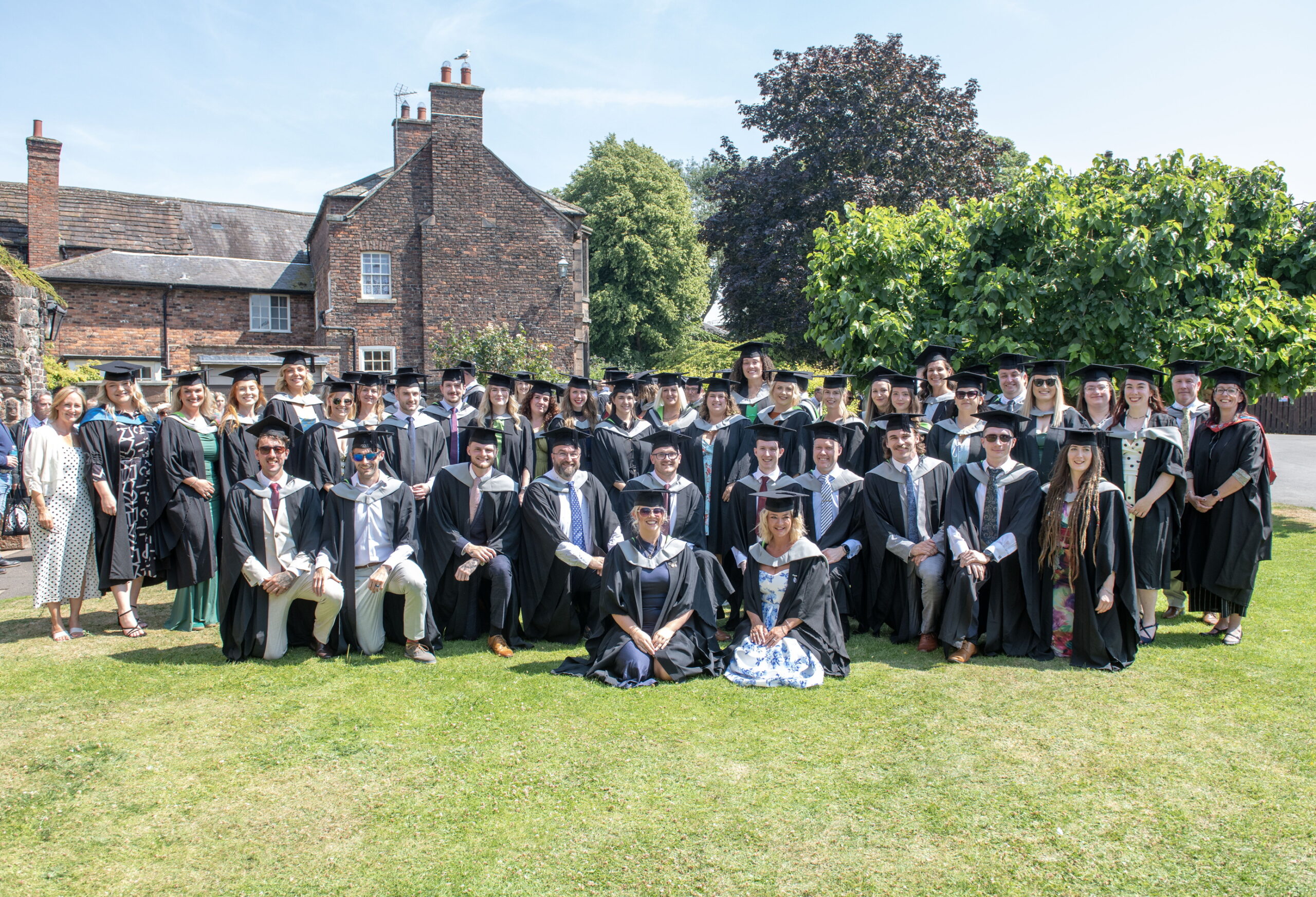 A group of graduates in traditional robes and mortar boards pose for a photo taken outside at their graduation ceremony